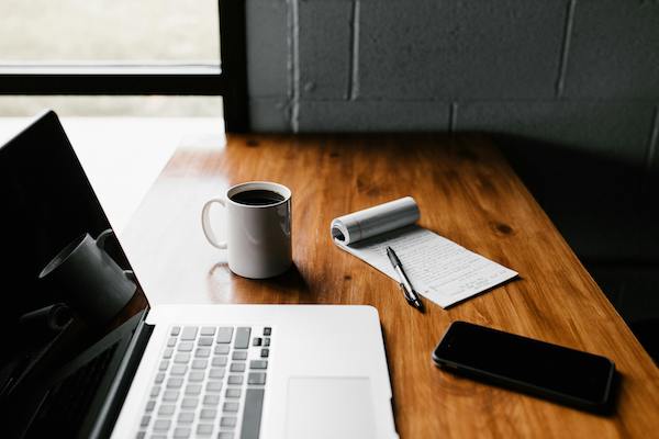 Calm workspace featuring a laptop, coffee mug, notepad, pen, and smartphone on a wooden desk, reflecting the intentional and collaborative spirit of PYM Connect.