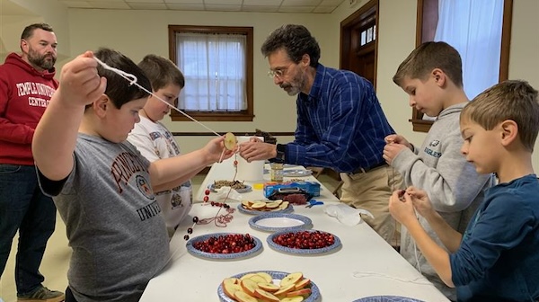 Children and adults creating fruit garlands together at a PYM Family Meetup, showcasing intergenerational activities and community building in a Quaker setting.