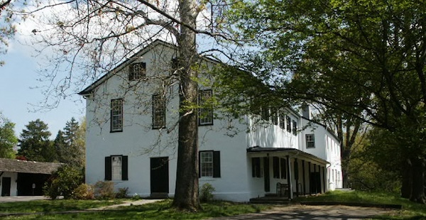 A photo of a white in color meetinghouse, the meetinghouse is Newtown Friends Meeting in Newtown, PA