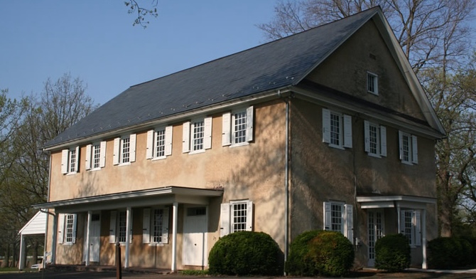 Quaker meetinghouse against blue sky, surrounded by trees.